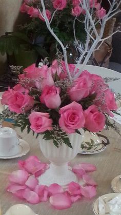 pink roses in a white vase on a table with teacups and saucers