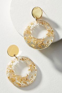 two pairs of gold and white earrings on top of a white surface with a circular disc