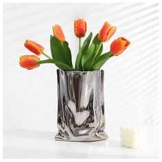 a vase filled with orange tulips on top of a white table next to a small marshmallow