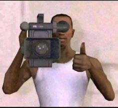 a man is holding a camera and giving the thumbs up while wearing a white tank top