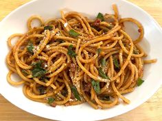 a white bowl filled with pasta and sauce on top of a wooden table next to a fork