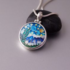 a pendant with an image of mountains and trees painted on the front is sitting on a rock