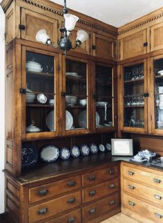 an old fashioned kitchen with wooden cabinets and glass front cupboards, including dishes on the counter