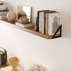 a shelf with books, vases and other items on it next to a wall