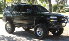 a large black truck parked on the side of a road next to a palm tree