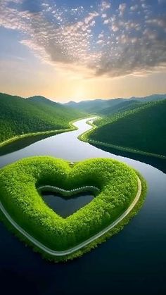 a heart shaped piece of grass in the middle of a river surrounded by hills and trees