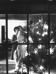 two women and a child standing in front of a christmas tree looking out the window