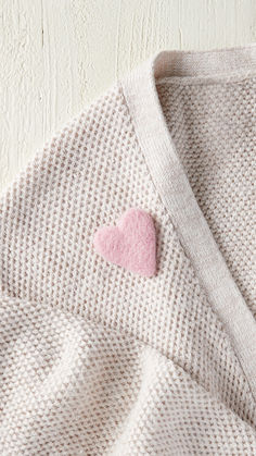 a sweater with a pink heart on the chest and a white wall in the background