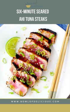 a white plate topped with sliced up meat next to chopsticks and a lime