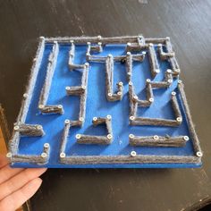 a hand is holding up a plastic model of a game board with metal parts on it