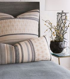 a close up of a bed with two pillows and a vase on the side table