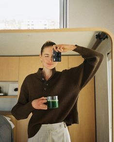 a woman taking a selfie in front of a mirror holding a camera and a cup