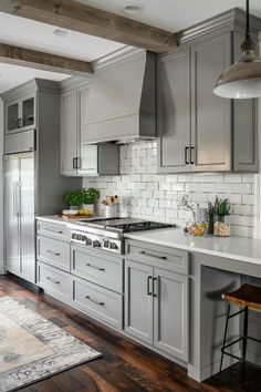 a kitchen with gray cabinets and white tile backsplash, wood flooring and an area rug