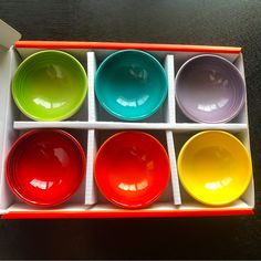 six different colored bowls in an open box on a black table with white trim around the edges