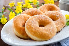 four donuts on a white plate with yellow flowers in the background