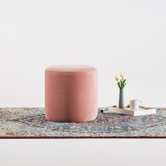 a pink stool with a plant on the floor next to it and a coffee cup