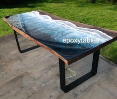 a table that is sitting on the ground in front of some grass and water with an ocean wave painted on it