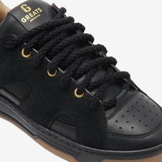 a black sneaker with gold accents and laces on the upper part of the shoe