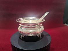 a glass bowl with spoons in it sitting on a black stand against a red background