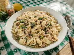 a white bowl filled with pasta and broccoli on top of a checkered table cloth