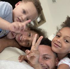 two children and an adult laying in bed making the peace sign with their hands while smiling