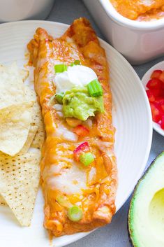 a white plate topped with an enchilada and tortilla next to two bowls of guacamole