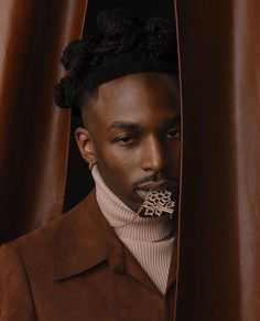 a man wearing a brown coat with his nose covered by a piece of fabric and looking out from behind the curtain