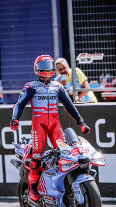 a man in red and blue racing suit standing next to a motorcycle