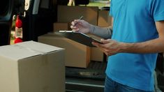 a man holding a clipboard in his hand next to a moving truck with boxes