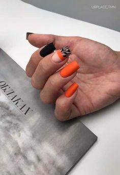 a woman's hand with orange and black nail polish on her nails next to a magazine