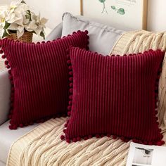 two red pillows sitting on top of a couch next to a vase with white flowers