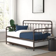 a metal day bed with blue sheets and pillows in a white room next to a window