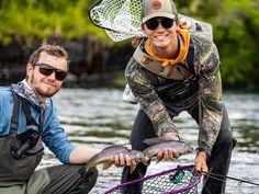 two men in waders holding fish on the water