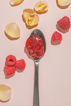 raspberries on a spoon with petals scattered around them