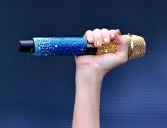 a woman holding a microphone up to her face with both hands and wearing gold bracelets