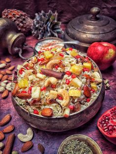 a bowl filled with fruit and nuts on top of a purple table covered in other food