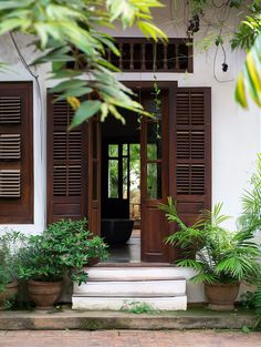 an open door to a white house with potted plants on the front steps and wooden shutters