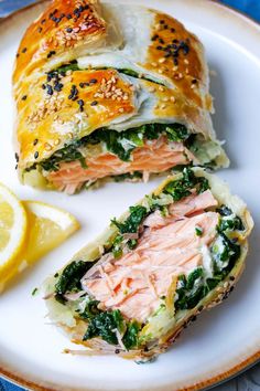 a sandwich with salmon and spinach is on a plate next to lemon wedges