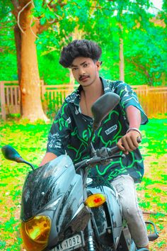 a man riding on the back of a motorcycle next to a green field and tree