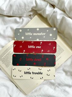 four little monsters bookmarks sitting on top of an open book laying on a bed