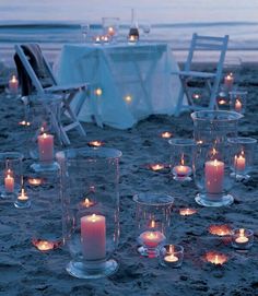 many lit candles are placed on the sand near chairs and tables with white linens