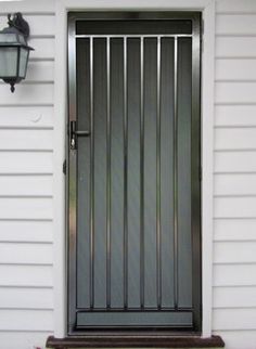 the front door of a white house with a black gate and light fixture on it