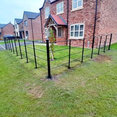 a black fence in front of a red brick house with grass and bushes around it