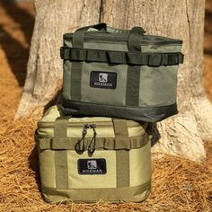 two cooler bags sitting next to each other on the ground near a tree and hay