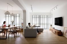 two people sitting on couches in a living room with a flat screen tv mounted to the wall