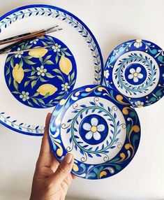 a hand holding three plates with yellow flowers on them and one blue plate that has lemons painted on it