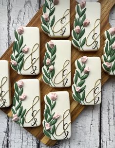 wedding cookies decorated with flowers and vines on a wooden cutting board next to the initials