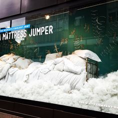 a window display with white bedding and pillows on it's sides, in front of a building