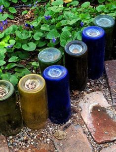 four blue and green vases sitting on the ground in front of some plants with purple flowers