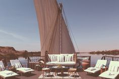 an outdoor deck with chairs, tables and couches on top of the deck next to water